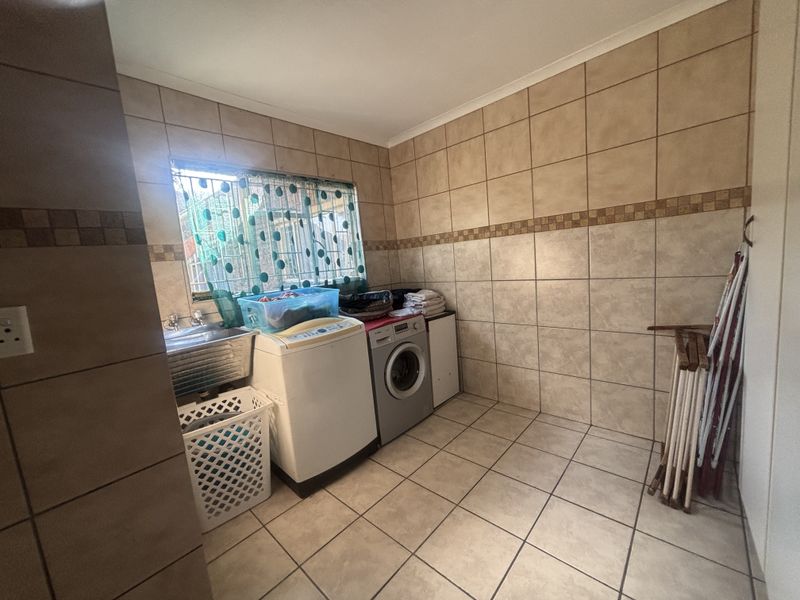 A functional laundry room featuring full-height wall tiling, floor tiles, and a built-in stainless steel utility sink with plumbing connections.