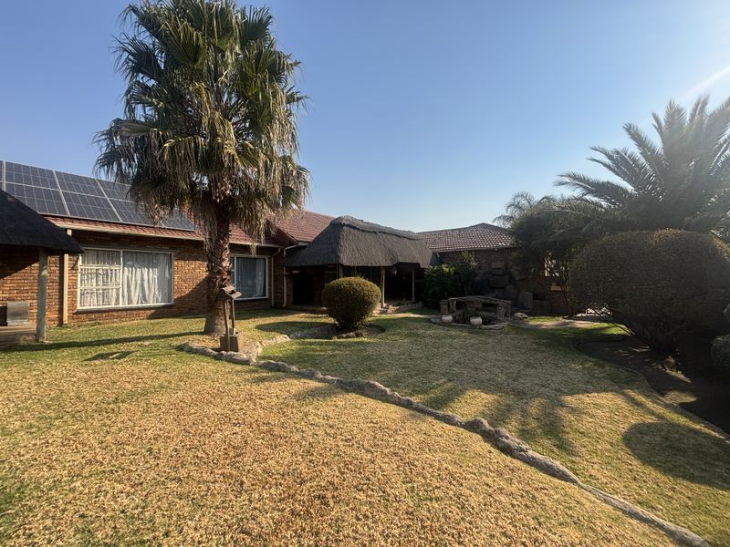 Spacious rear garden featuring a brick house with solar panels, a thatched roof area, and established landscaping.