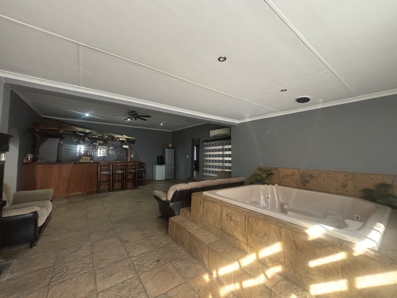 Spacious open-plan entertainment area featuring a built-in bar, a raised tiled spa bath, and neutral grey walls with tiled flooring throughout.