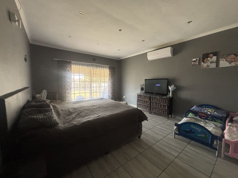 Spacious bedroom featuring tiled flooring, recessed downlighting, and a wall-mounted split-system air conditioner with direct access to the exterior.