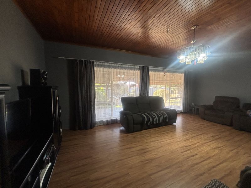 Spacious living room featuring a warm timber-clad ceiling, laminate flooring, and large sliding glass doors that provide ample natural light and garden access.