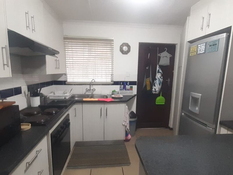 A functional kitchen featuring white cabinetry, dark laminate countertops, a built-in oven with hob, and a double basin sink with window views.