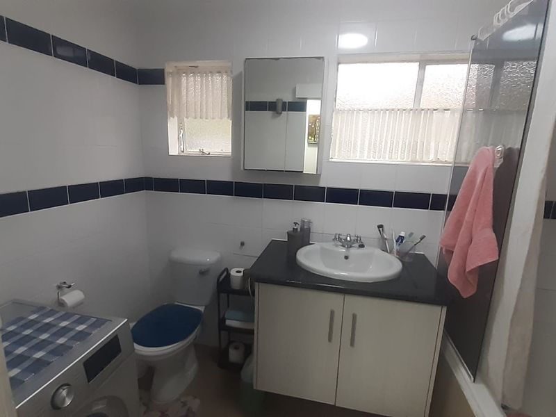 A functional bathroom featuring a vanity cabinet, basin, toilet, and shower area with classic tiled wall accents.