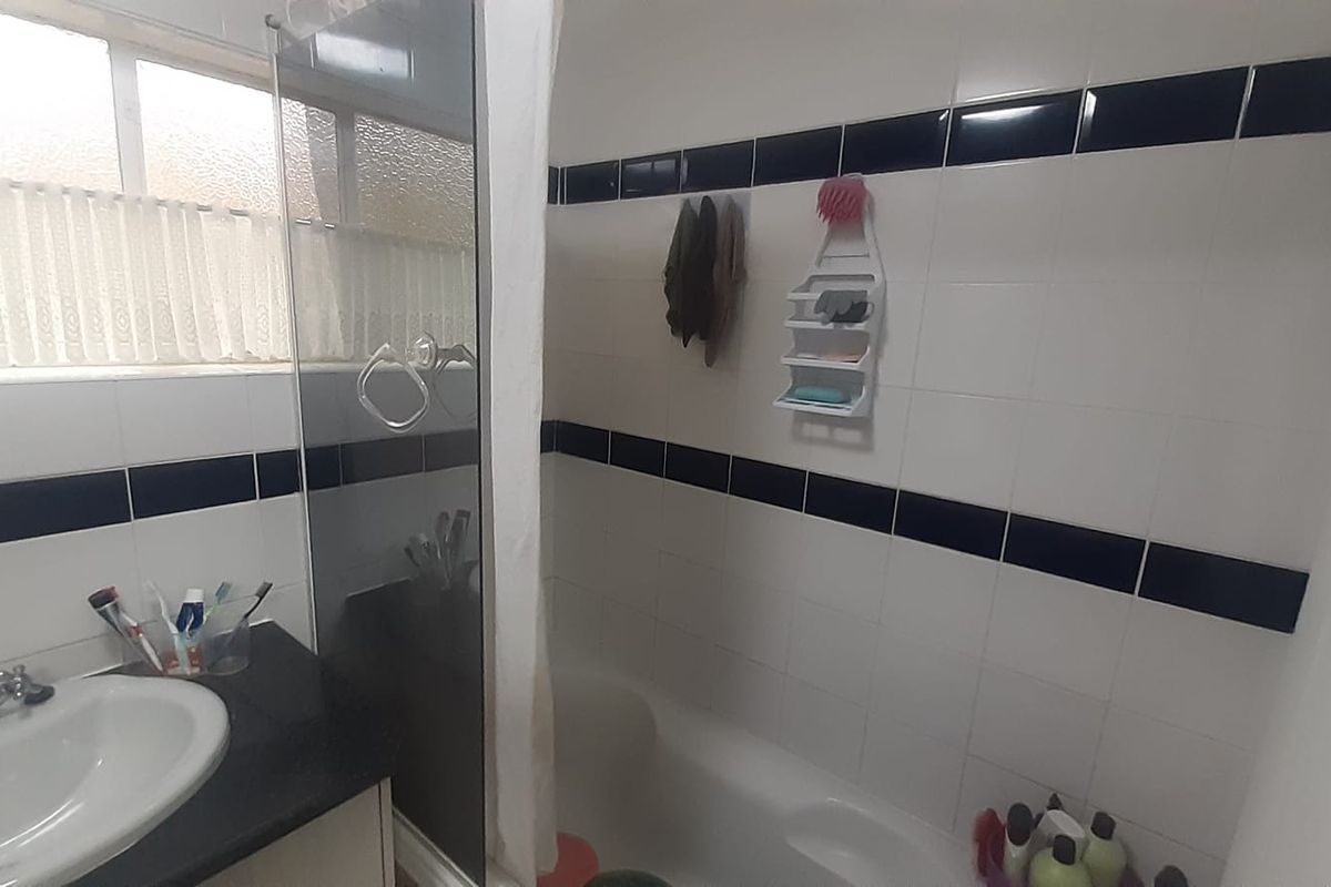 A functional bathroom featuring a built-in vanity with basin, a combined shower and bathtub area, and classic black and white tiled wall accents.