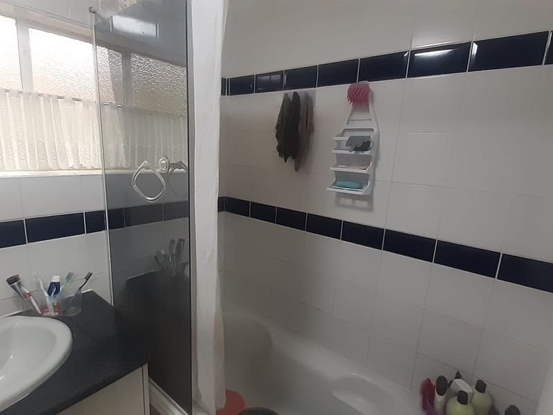 A functional bathroom featuring a built-in vanity with basin, a combined shower and bathtub area, and classic black and white tiled wall accents.