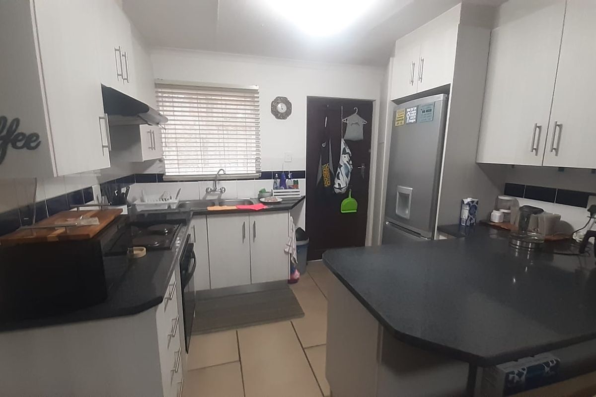 Functional kitchen featuring white cabinetry, dark countertops, tiled backsplash, and a breakfast bar area with direct access to an exterior door.