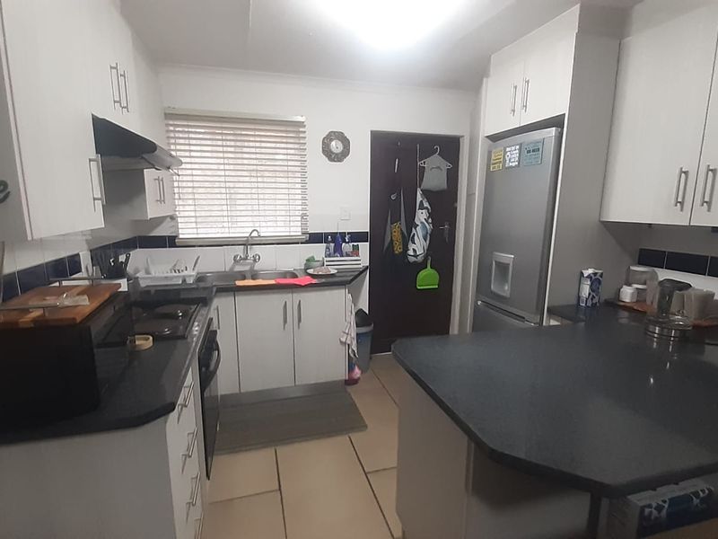 Functional kitchen featuring white cabinetry, dark countertops, tiled backsplash, and a breakfast bar area with direct access to an exterior door.