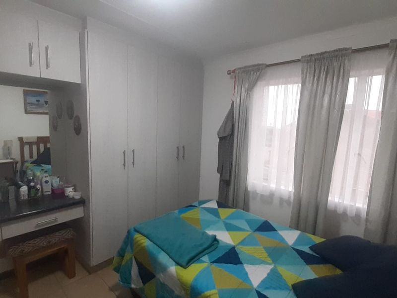 A functional bedroom featuring built-in cupboards and a matching built-in vanity unit with tiled flooring and natural light from the window.