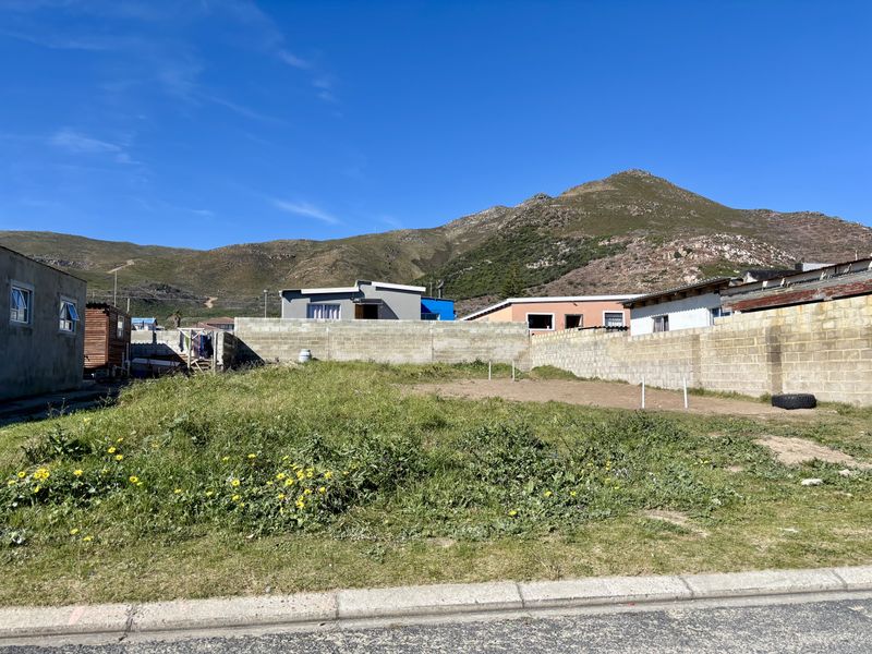A vacant residential plot enclosed by concrete block perimeter walls, featuring mountain views and direct street access.