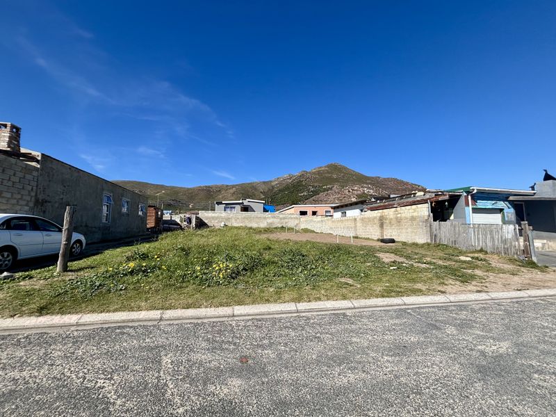 A vacant residential plot featuring a concrete block boundary wall, situated in a neighborhood with mountain views.