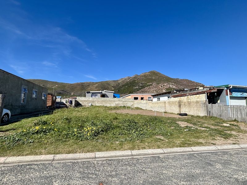 A vacant residential plot featuring a perimeter boundary wall and street frontage, set against a scenic mountain backdrop.