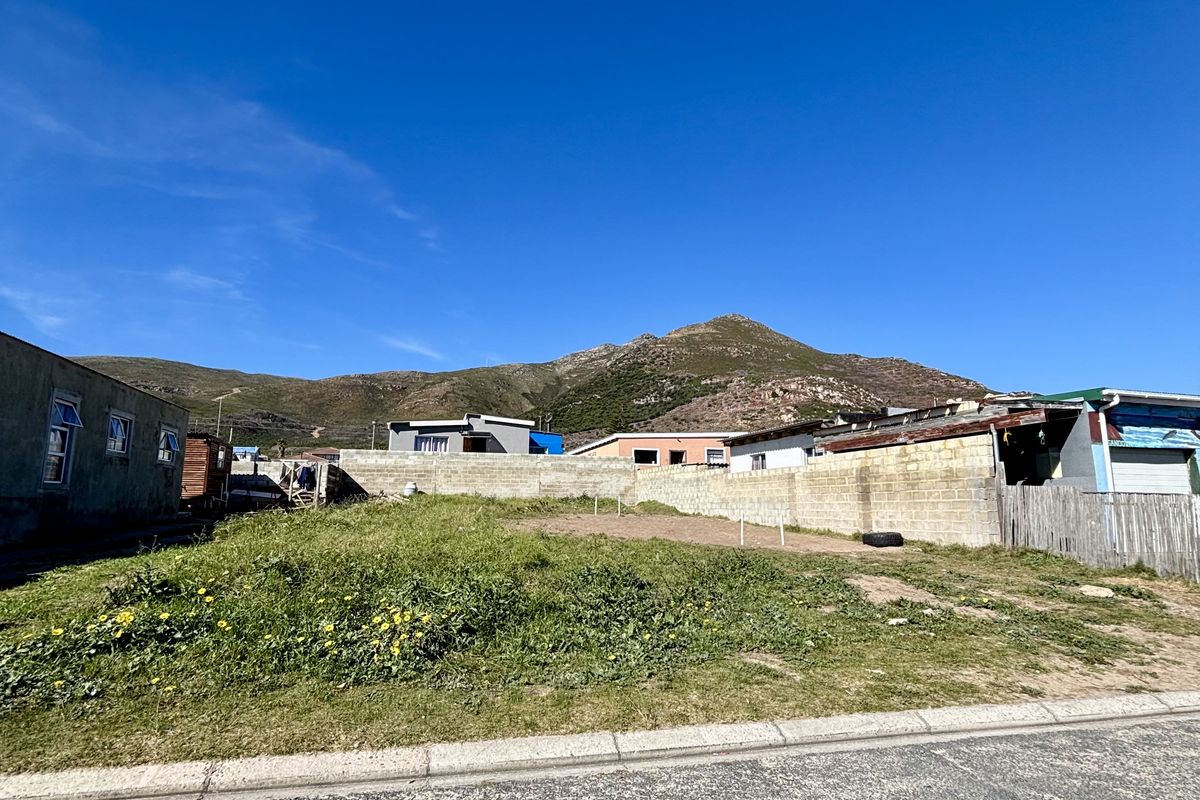 A vacant residential plot featuring a boundary wall, street frontage, and mountain views in the background.