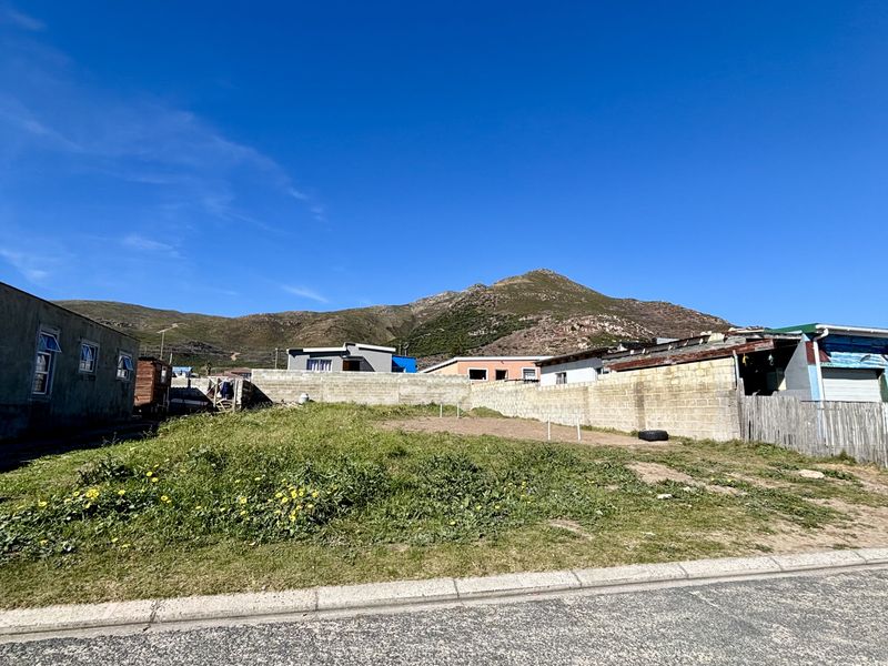 A vacant residential plot featuring a boundary wall, street frontage, and mountain views in the background.