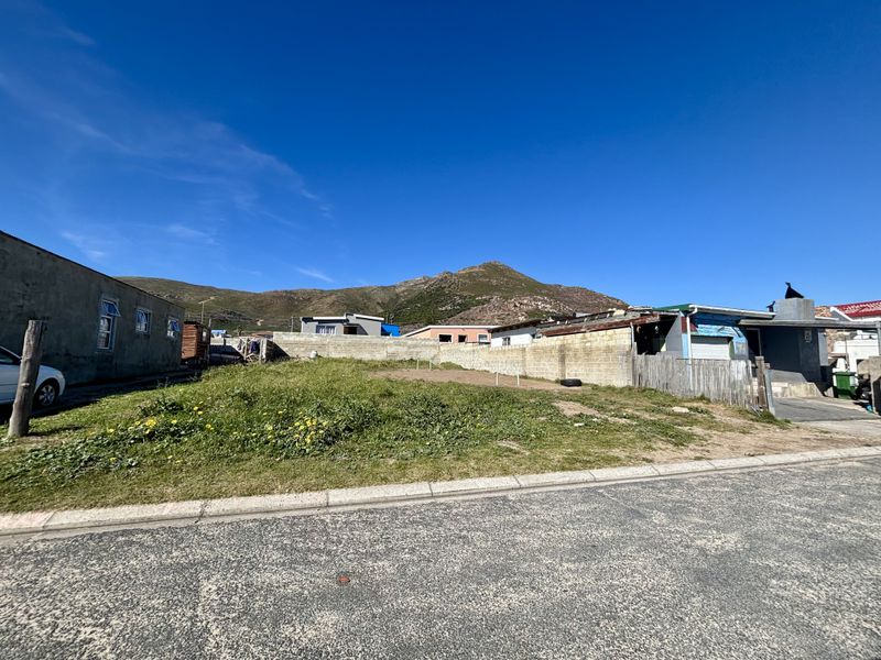 A vacant residential plot featuring a boundary wall and street access, situated in a neighborhood with mountain views.