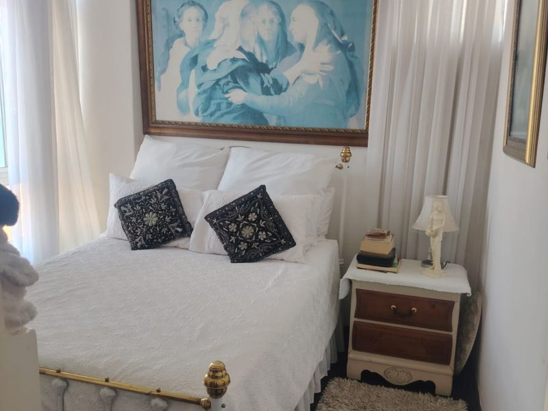 A compact bedroom featuring neutral walls, sheer curtains, and a central pendant light fixture.
