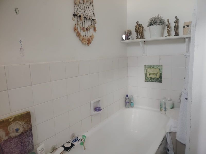 A functional bathroom featuring a built-in bathtub with white wall tiling, a recessed soap niche, and a wall-mounted storage shelf.