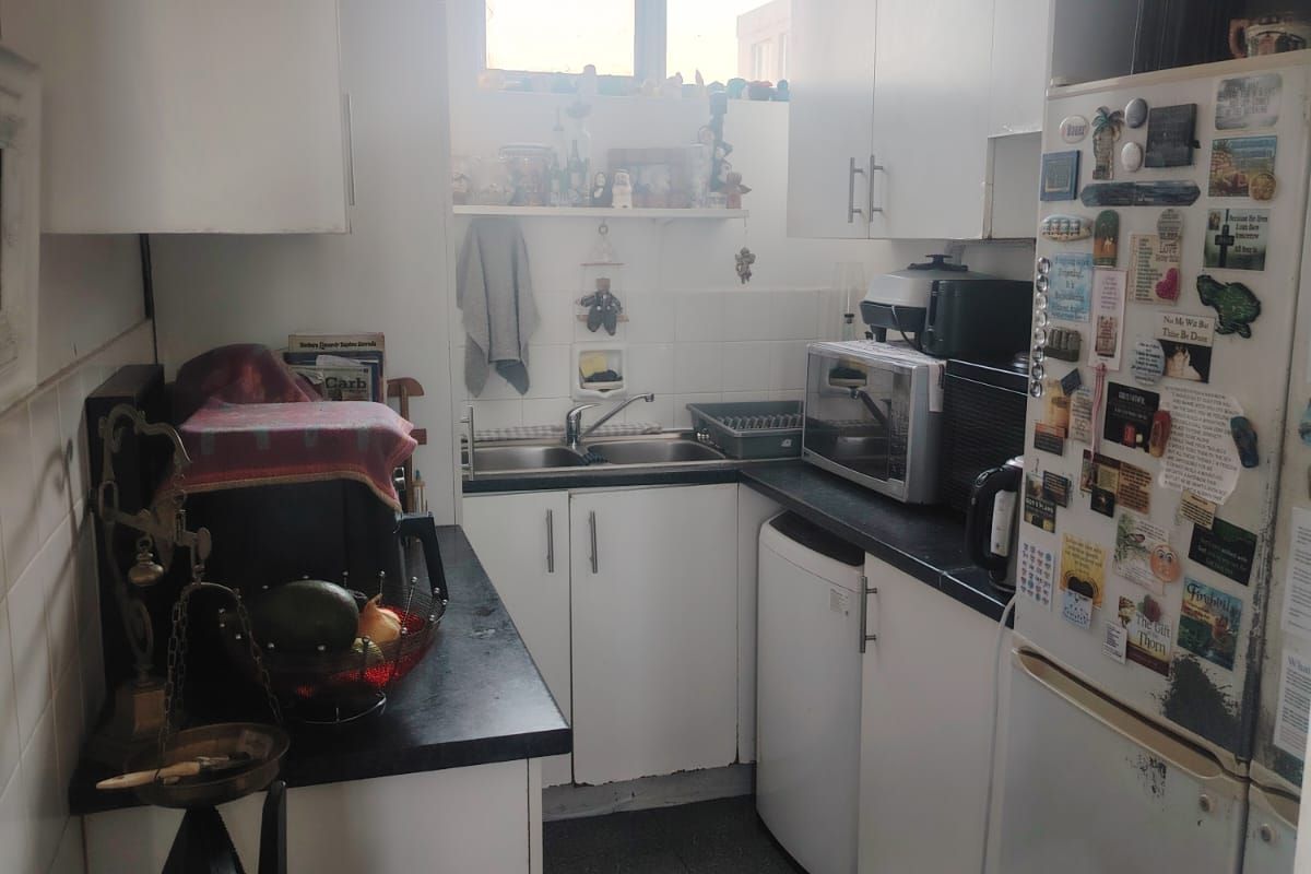 A compact galley-style kitchen featuring white cabinetry, dark countertops, and a stainless steel sink, offering a functional layout with potential for modernization.