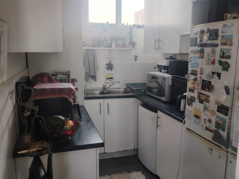 A compact galley-style kitchen featuring white cabinetry, dark countertops, and a stainless steel sink, offering a functional layout with potential for modernization.