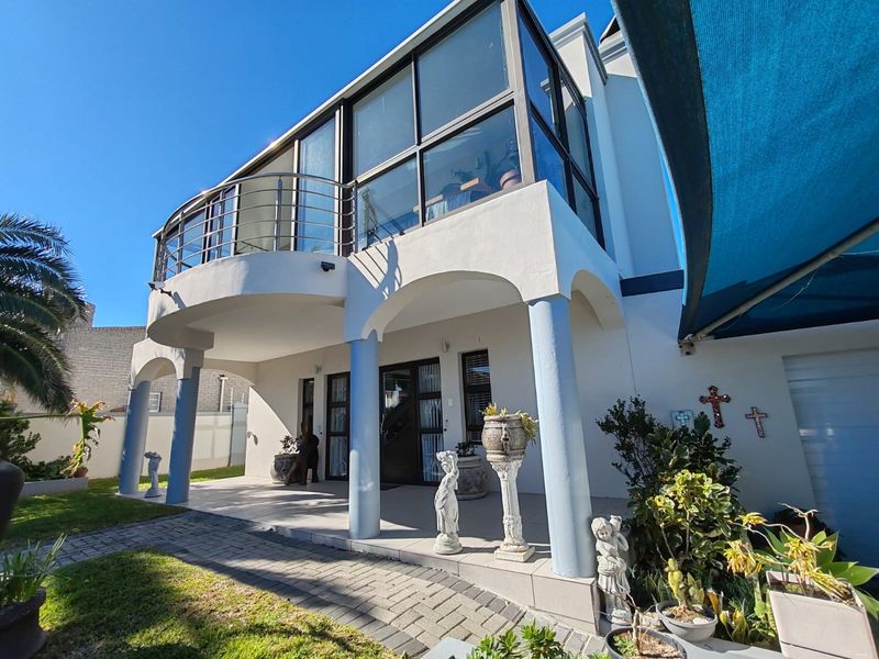 Rear exterior view featuring a covered patio, paved walkway, and an upper-level enclosed balcony with stainless steel balustrades.