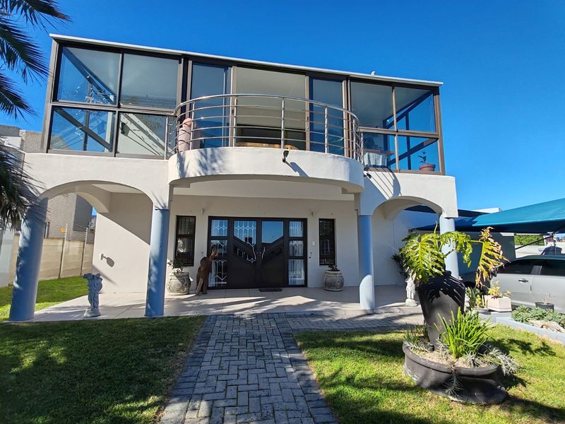 Front elevation of a two-story house featuring a paved walkway, arched pillars, and an upper-level balcony with a stainless steel balustrade.