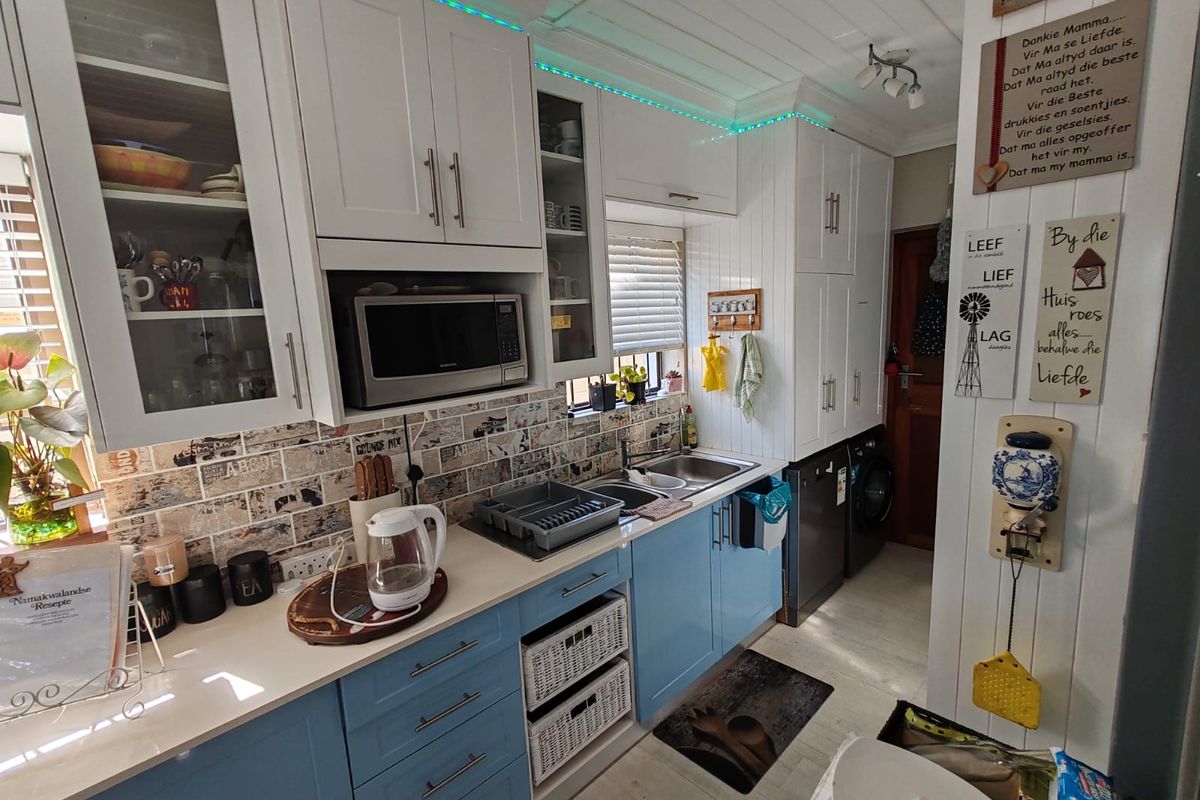 A functional kitchen featuring white and blue cabinetry, a tiled backsplash, built-in microwave, and double sink with integrated laundry space.
