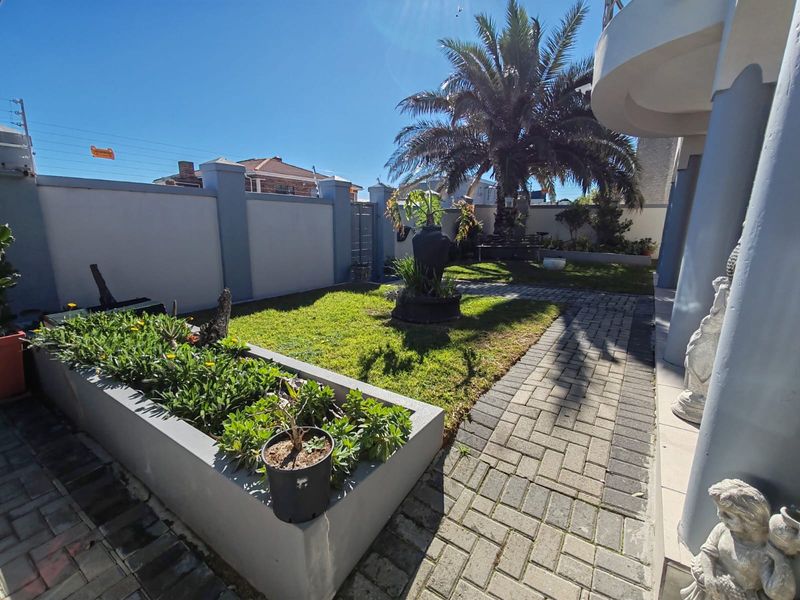 A well-maintained garden area featuring a paved walkway, raised planter boxes, and solid boundary walls with structural pillars.