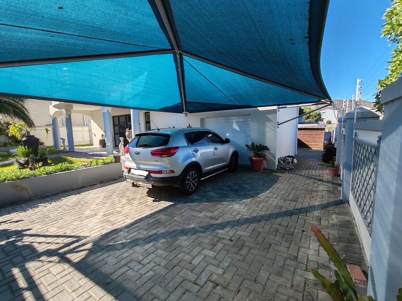 Front exterior view featuring a paved driveway, a blue shade sail structure, and access to the garage.