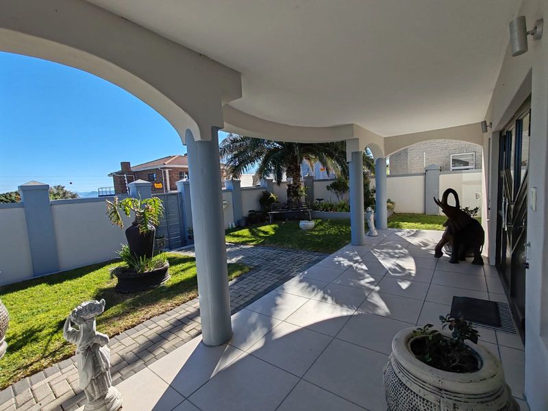 A covered patio area featuring tiled flooring and arched columns, overlooking a well-maintained garden with paved pathways and boundary walls.