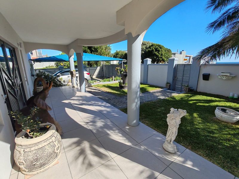 A covered patio area featuring tiled flooring and concrete columns, overlooking a well-maintained garden with a paved walkway and boundary wall.