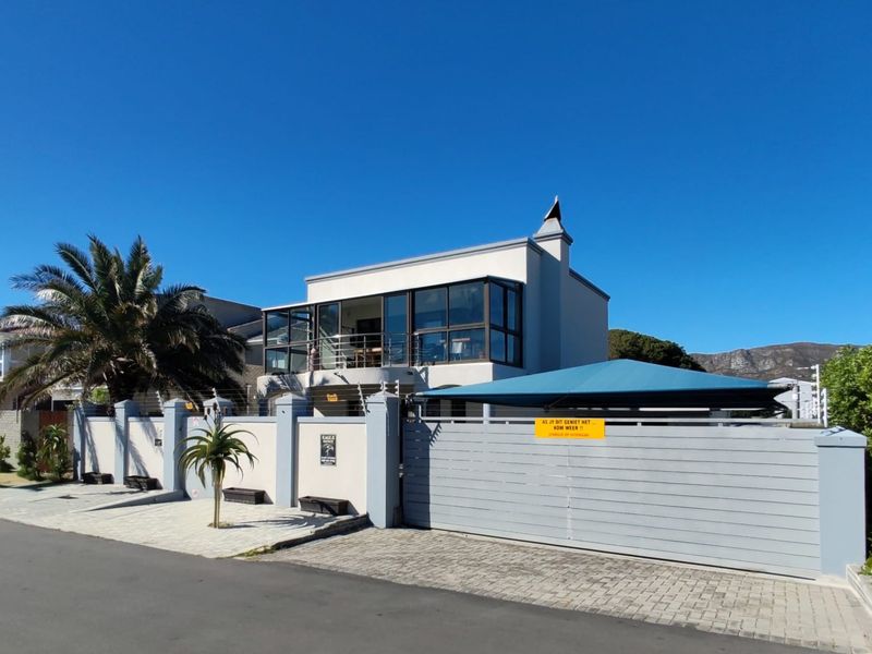 Front exterior view of a modern two-story house featuring a paved driveway, secure boundary wall with electric fencing, and an upper-level balcony.