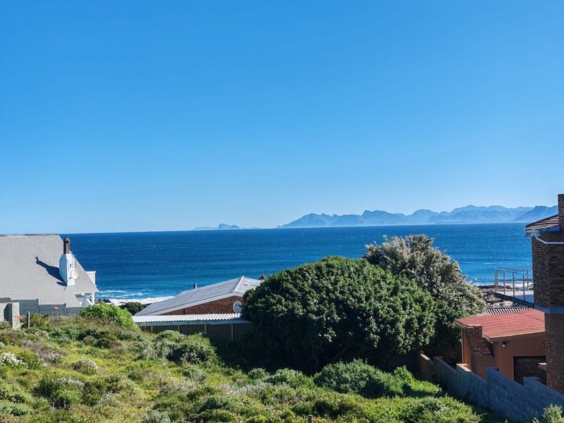 A scenic elevated view overlooking the ocean and distant mountain range, capturing the coastal landscape and surrounding residential rooftops.