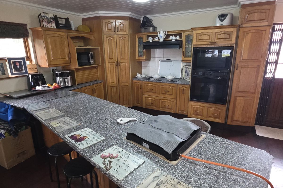 A traditional kitchen featuring extensive wooden cabinetry, granite countertops, a built-in oven, and timber flooring, offering a functional layout with ample storage space.