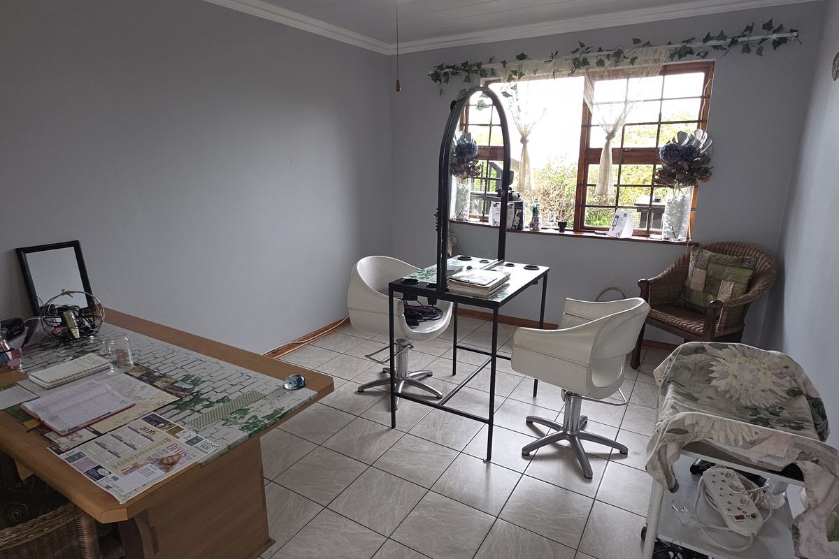 A functional room currently utilized as a workspace, featuring tiled flooring, neutral wall paint, and a window with security bars.