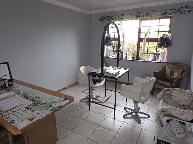 A functional room currently utilized as a workspace, featuring tiled flooring, neutral wall paint, and a window with security bars.
