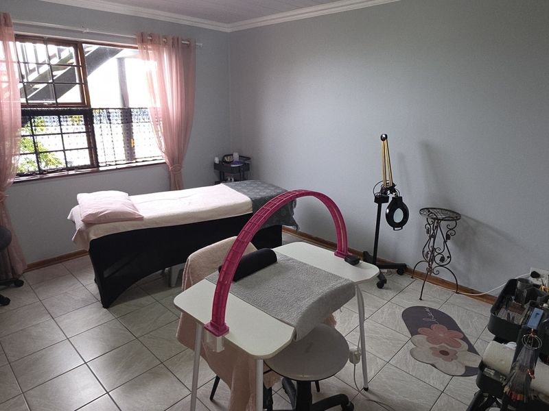 A functional bedroom space featuring tiled flooring, crown molding, and a window fitted with security bars, currently utilized as a beauty treatment room.