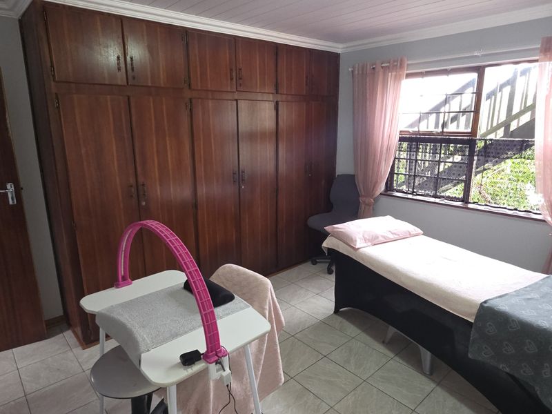 A bedroom featuring built-in wooden cupboards, tiled flooring, and a window with natural light, currently utilized as a treatment room.