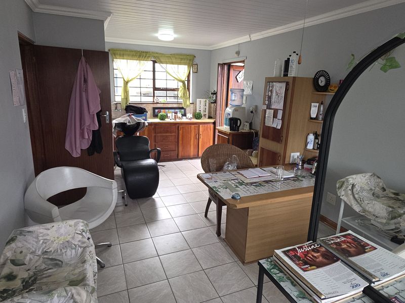A functional utility space featuring tiled flooring, built-in wooden cabinetry, and a window with security bars, currently utilized as a salon area.