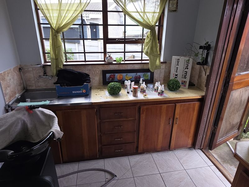 A functional utility or salon prep area featuring built-in wooden cabinetry, a stainless steel sink, and tiled finishes with direct outdoor access.