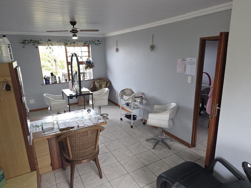 A functional utility space currently utilized as a salon, featuring tiled flooring, a ceiling fan, and natural light through a window with security bars.