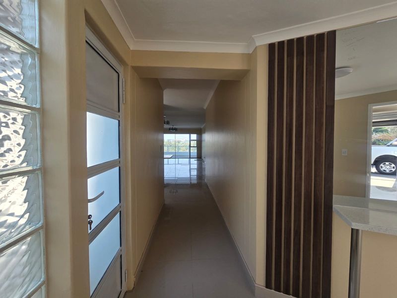 Entrance hallway featuring tiled flooring, a decorative slatted wood feature wall, and a glass block wall, leading through to an open-plan living area.