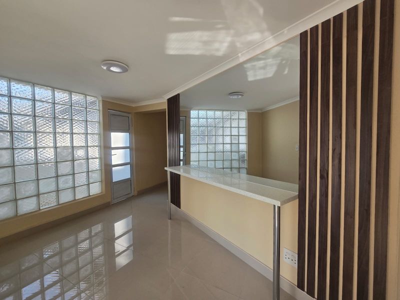 A bright, modern living area featuring a built-in bar counter, decorative timber slat paneling, a large mirror, and unique glass block wall detailing.