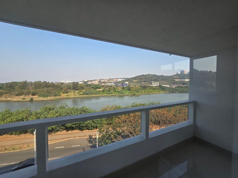 A spacious balcony featuring a concrete balustrade and tiled flooring, offering expansive views of the river and surrounding landscape.