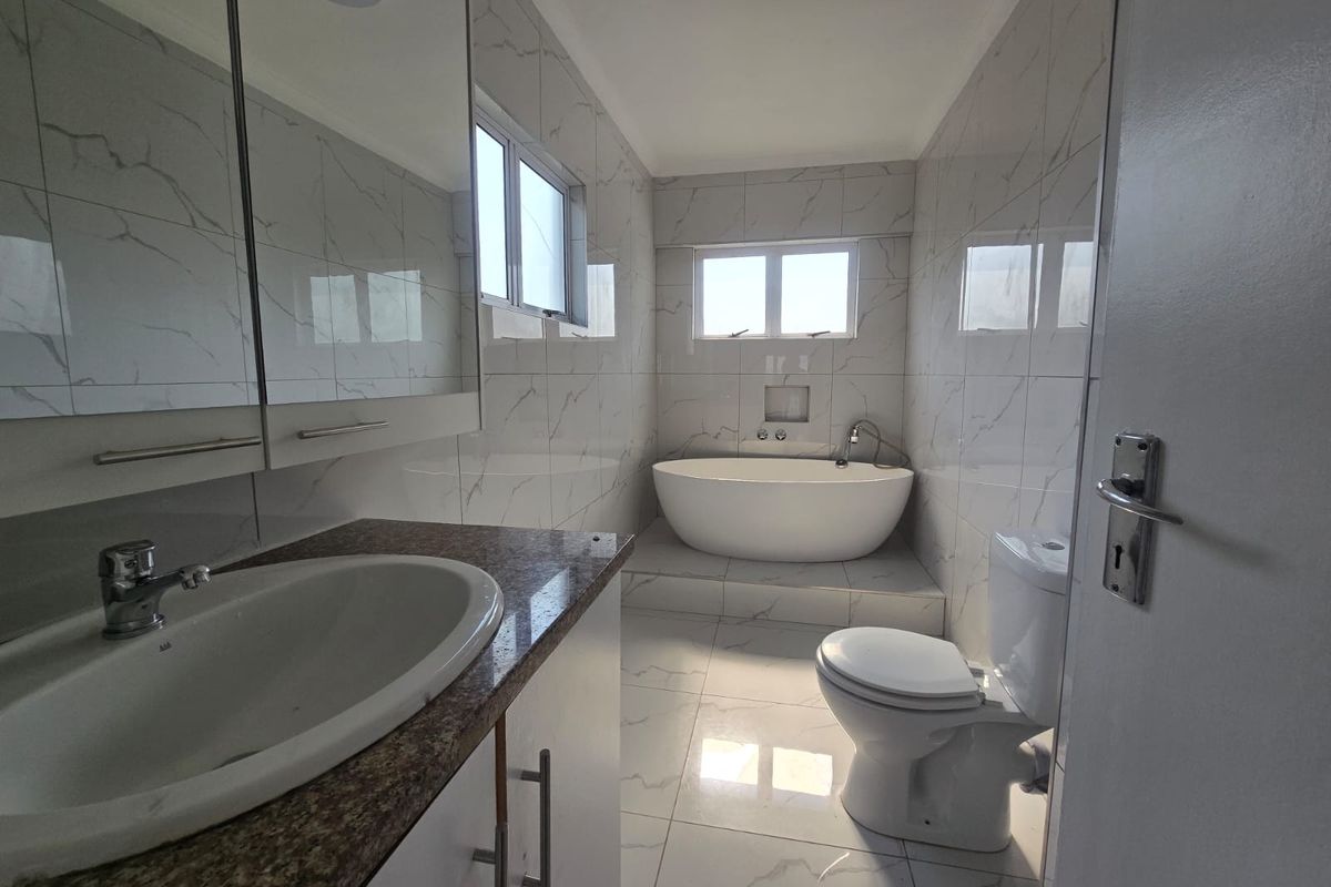 Modern, well-maintained bathroom featuring a freestanding bathtub, vanity with granite countertop, and elegant marble-look tiling throughout.