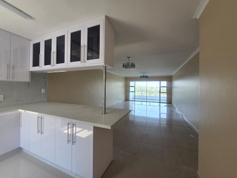 Spacious open-plan kitchen and living area featuring modern white cabinetry, stone countertops, tiled flooring, and large sliding doors leading to a balcony.