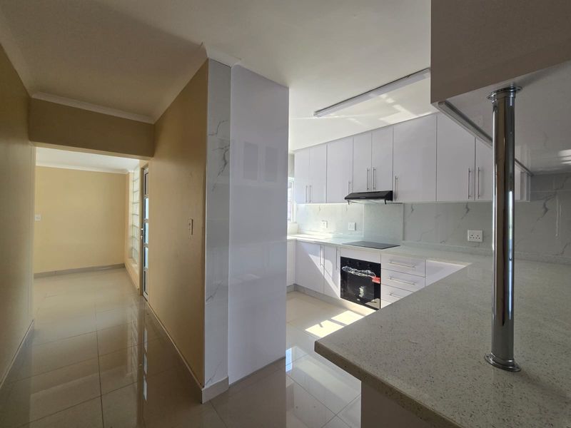 Modern kitchen featuring white cabinetry, stone countertops, integrated appliances, and sleek tiled flooring, seamlessly connected to an adjacent hallway.