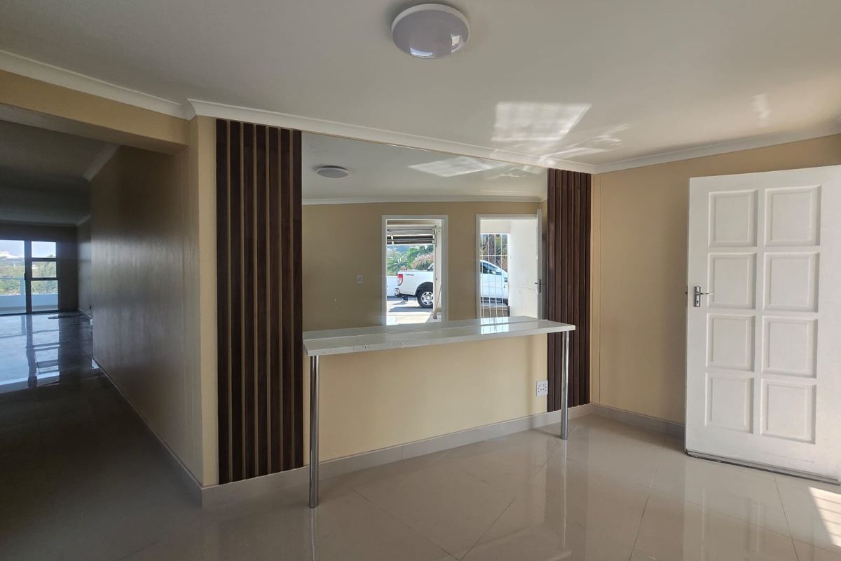 An open-plan living area featuring a built-in breakfast bar, decorative wood-slat wall paneling, a large mirror, and neutral tiled flooring.