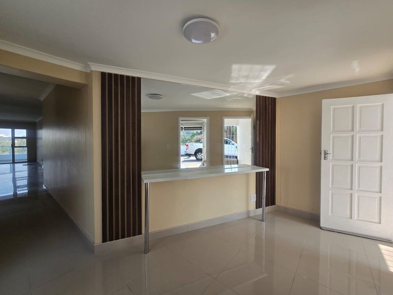 An open-plan living area featuring a built-in breakfast bar, decorative wood-slat wall paneling, a large mirror, and neutral tiled flooring.