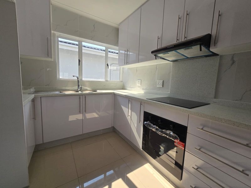 Modern kitchen featuring white high-gloss cabinetry, stone countertops, integrated electric hob, oven, extractor fan, and marble-look splashback with tiled flooring.