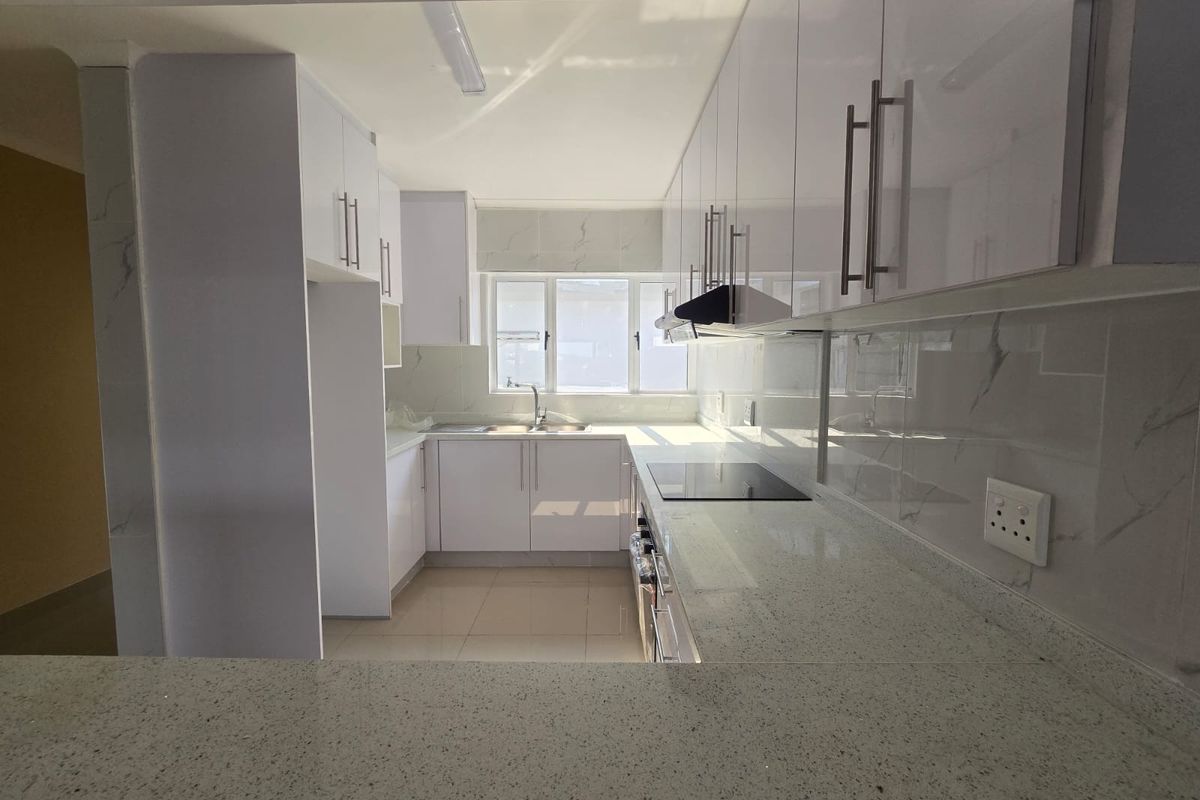 A modern, clean kitchen featuring white gloss cabinetry, stone countertops, integrated hob, and extractor fan, offering a bright and functional workspace.