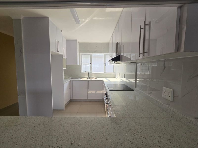 A modern, clean kitchen featuring white gloss cabinetry, stone countertops, integrated hob, and extractor fan, offering a bright and functional workspace.